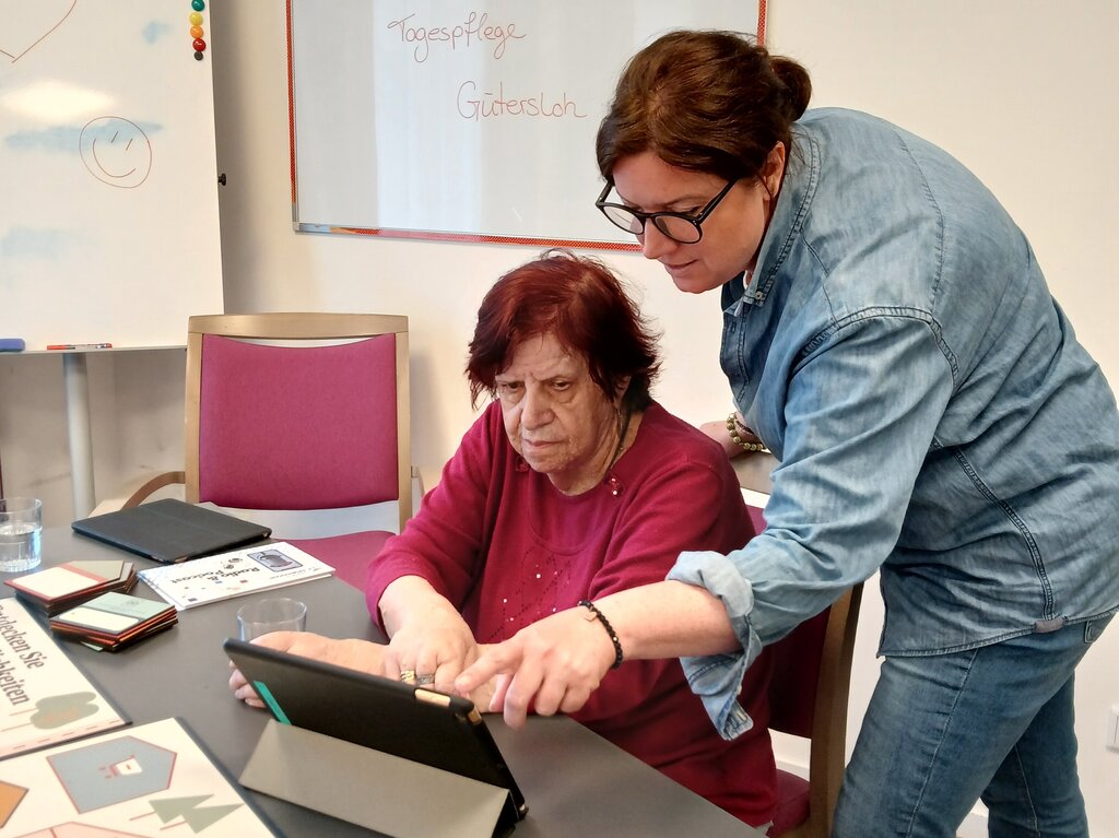 Eine Frau zeigt einer älteren Dame, wie man ein Tablet benutzt.