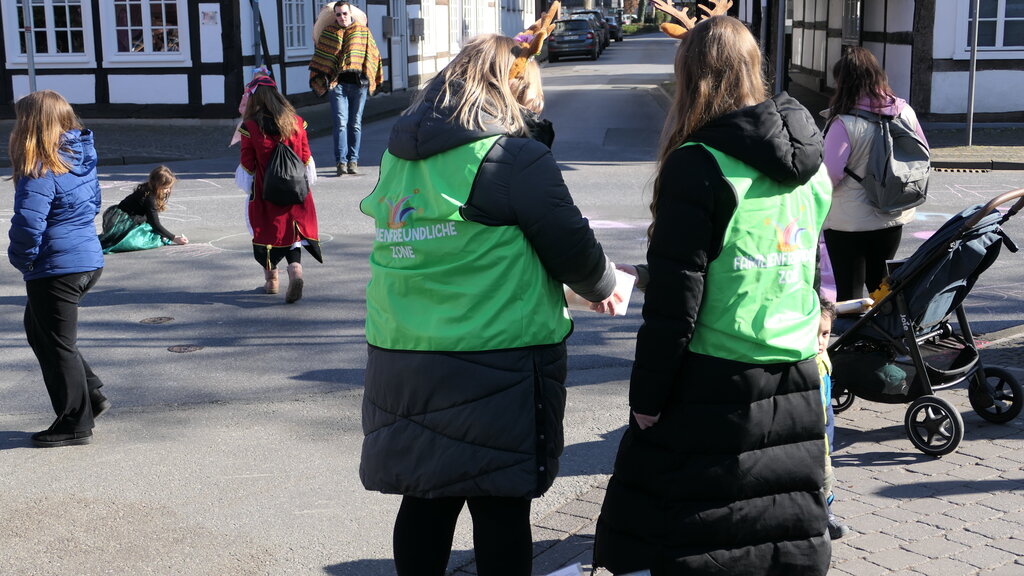 Kinder malen mit Straßenkreide und zwei Mitarbeiterinnen der Familienfreundlichen Zone verteilen Straßenkreide.
