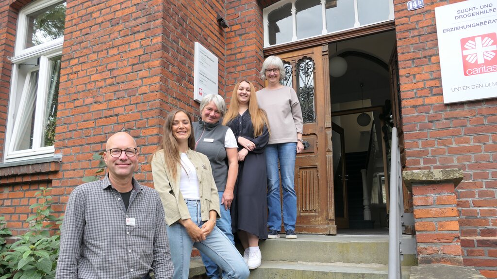 Ein Mann und zwei Frauen stehen auf der Eingangstreppe zu einem Caritas--Haus.