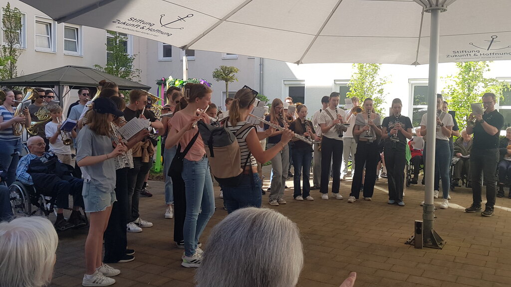 Junge Blasmusiker spielen unter einem großen Sonnenschirm ein Konzert für Senior:innen