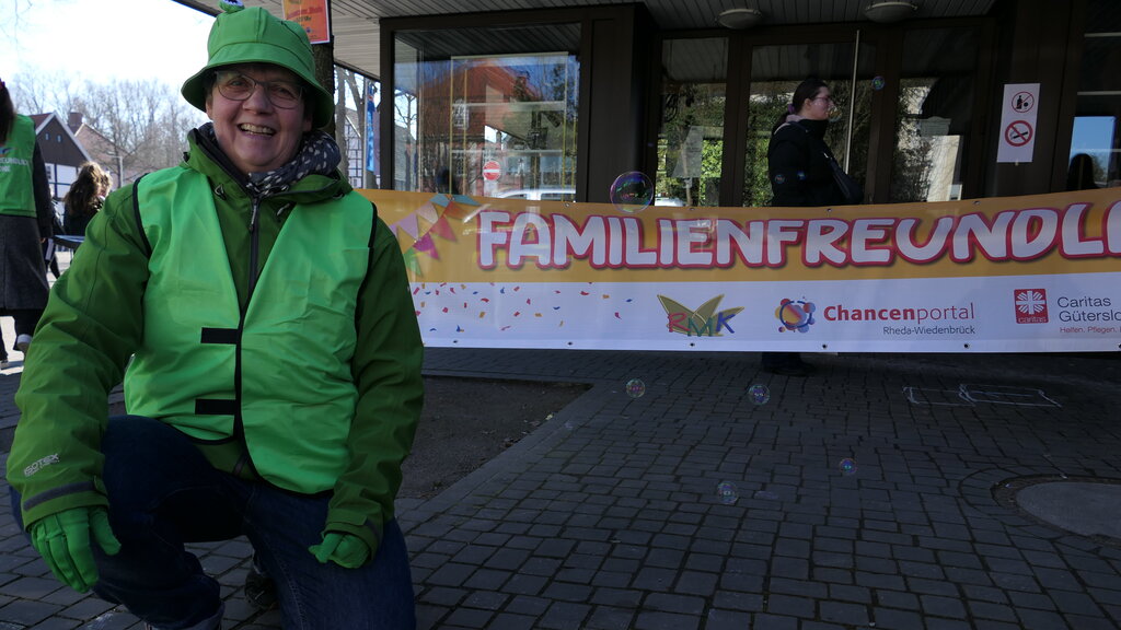 Caritas-Mitarbeiterrin kniet vorm Banner der Familienfreundlichen Zone in Rheda.